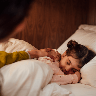 Parent tucking child into bed