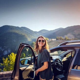 Middle-age woman stands in open car door in workout clothes with mountain in the background