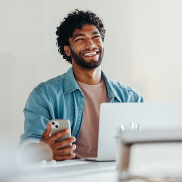 Young professional sitting at laptop with phone in hand