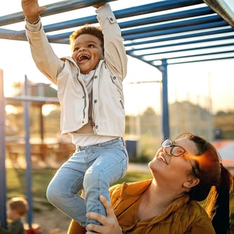 Mom holding son as he swings across jungle gym