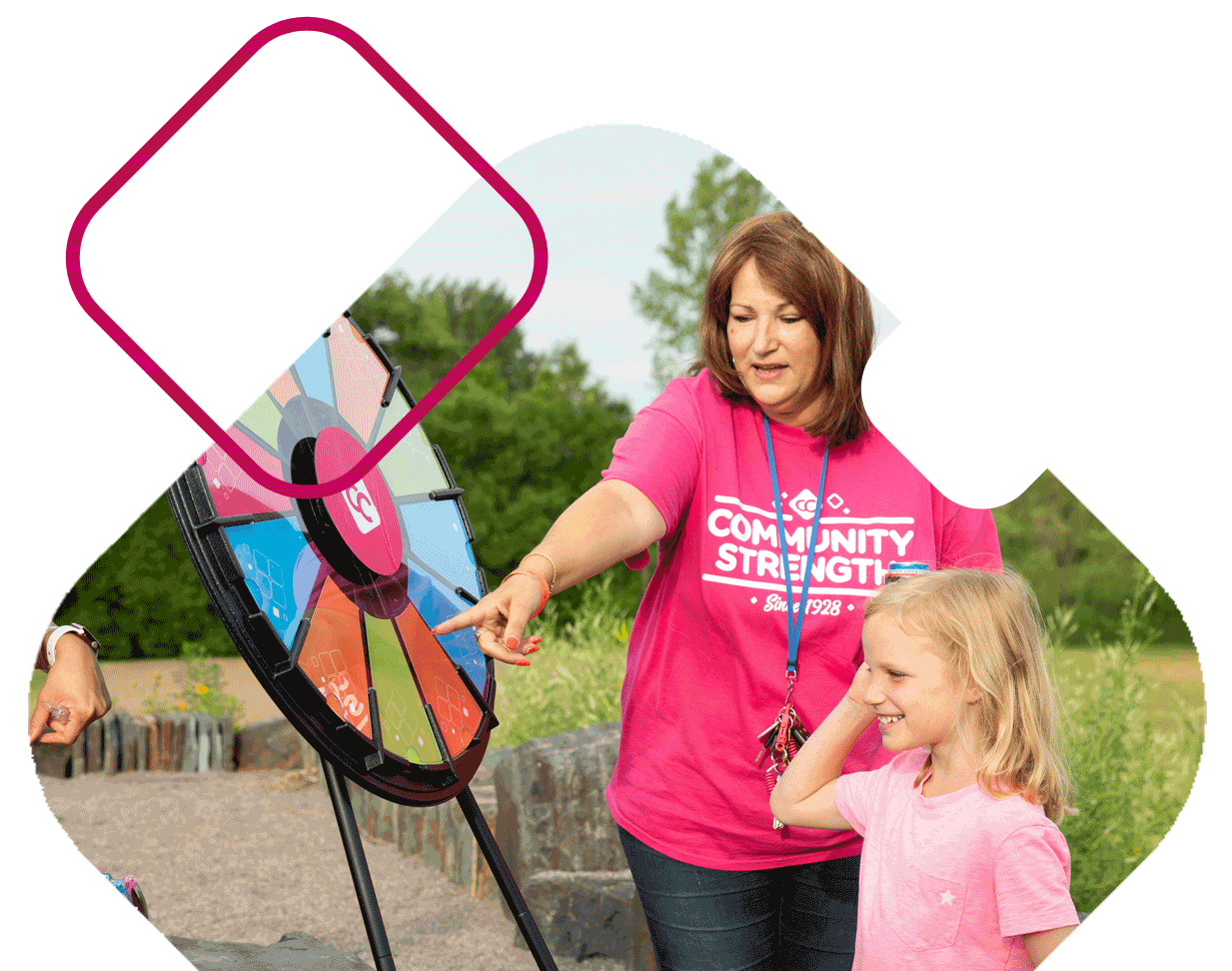 Woman wearing pink CCCU shirt points at spinwheel next to young girl smiling.