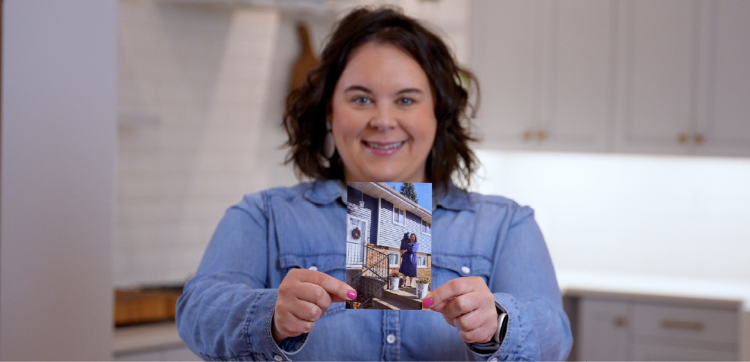 Member Brittany holds up photo of new house and smiles at camera.
