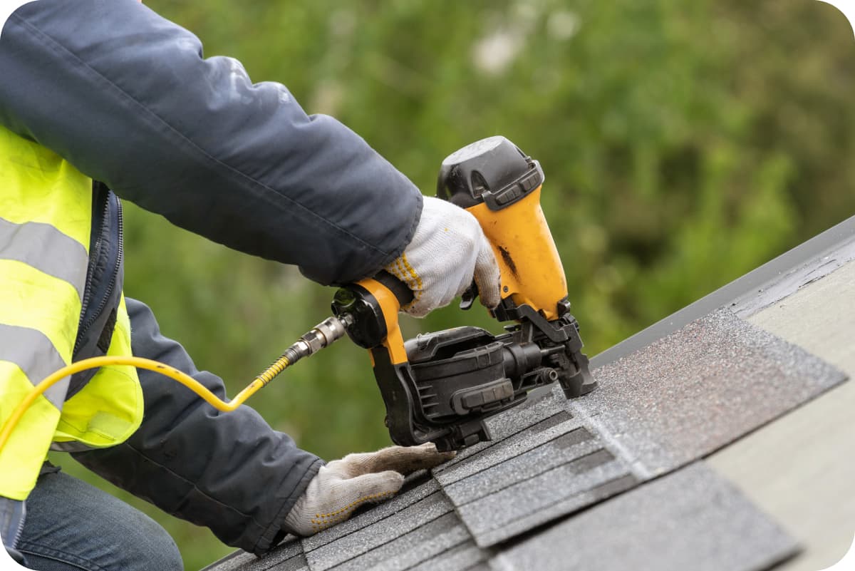 worker-using-pneumatic-nail-gun-installing-roofing-shingles