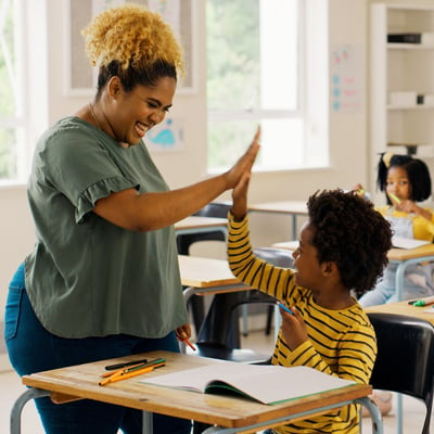 teacher high-fiving student in classroom